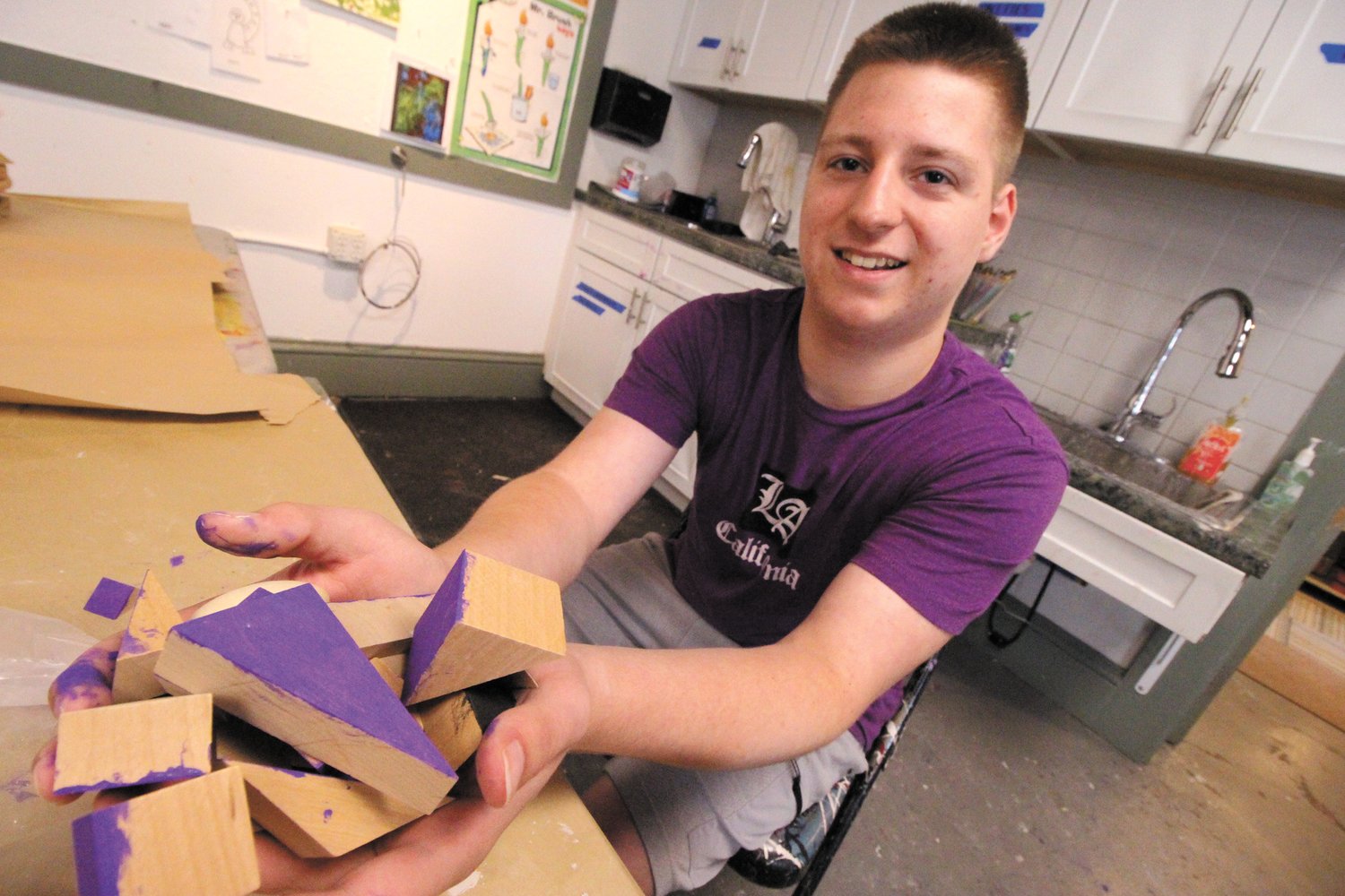 HELPING OUT: Coventry High School student Aiden Petrin has been volunteering at the summer art camp. Last week he assisted by painting one surface on scores of different shaped wooden blocks that campers will use for their projects. The color he picked? Well, purple of course – it’s is favorite.